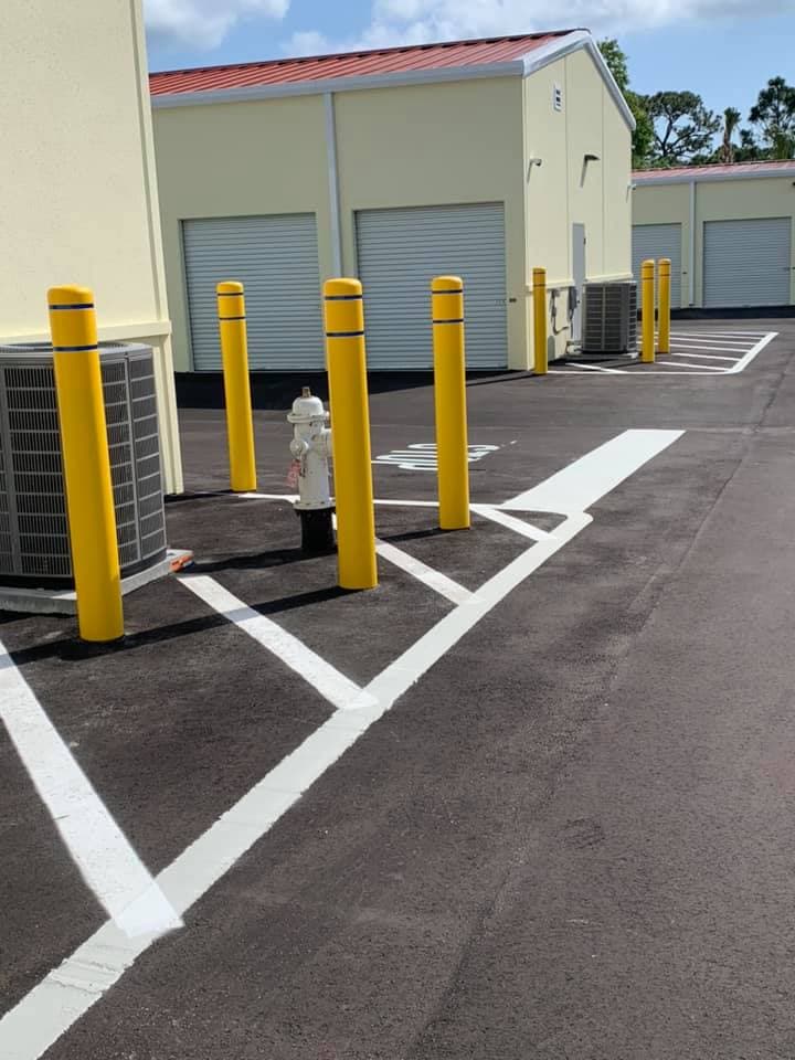 Freshly painted yellow safety bollards protecting a fire hydrant and utility equipment in a striped parking area