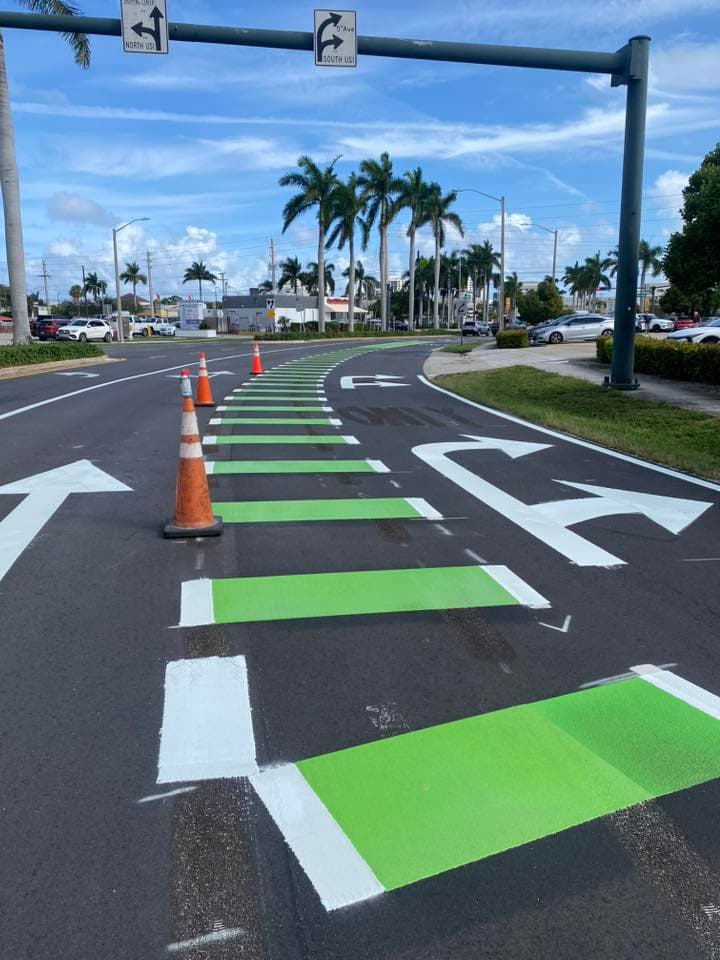 Freshly painted white turn-lane arrows and green-highlighted crosswalk on a Florida roadway